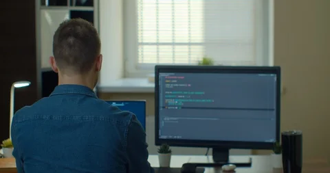 Young man freelancer coding html and programming on two screen Monitors Stock Footage 129449308