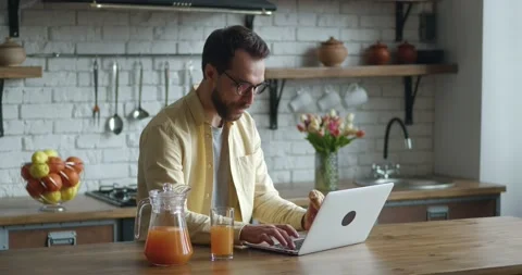Young man freelancer in eyeglasses working at laptop computer and eating tasty Stock Footage 196941622