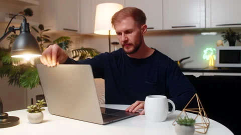Young man freelancer opens laptop at evening starts remote work drinks hot tea Stock Footage 327042568