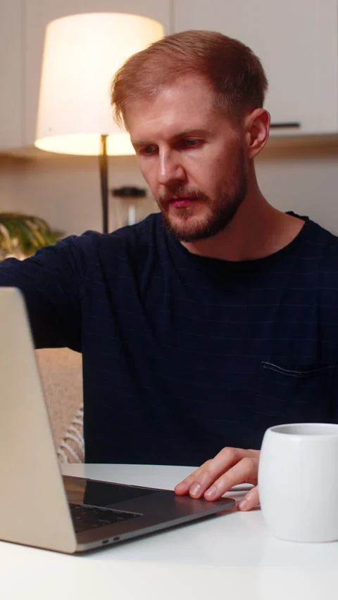 Young man freelancer opens laptop at evening starts remote work drinks hot tea Stock Footage 347553416