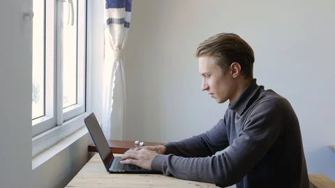Young man freelancer using laptop, typing, scrolling, surfing web, looking at Stock Footage 129007240