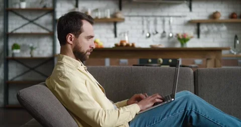 Young man freelancer using laptop device while resting on sofa at home, portrait Stock Footage 196940389