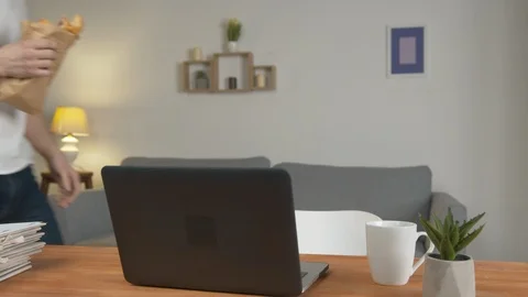 Young man freelancer work at home and eating on a desk with laptop, looks at a 스톡 동영상 127433306