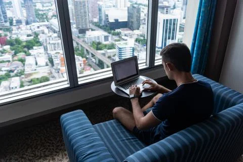 Young man freelancer working at home with laptop. Panoramic windows Stock Photos