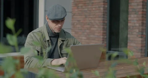 Young man freelancer working with laptop sitting in outdoor cafe concentrated on Stock Footage 256560500