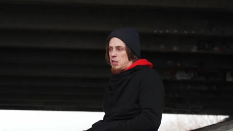 A young man with a friendly smile relaxes under an urban bridge on a cloudy day Stock Footage 293093629