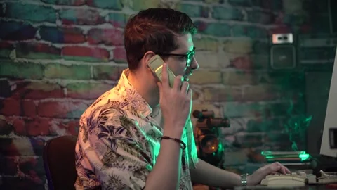 Young Man in Front of Desktop Computer Answering Phone Call on Mobile From Video stock 305571175
