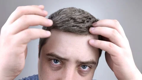 A young man in front of a mirror examines his early gray hair. The concept of ea Stock Footage 126407445