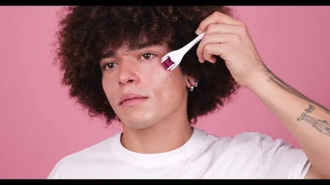 A young man with full, visible tattoos on his arm holds a derma roller to his Stock Footage 269136806