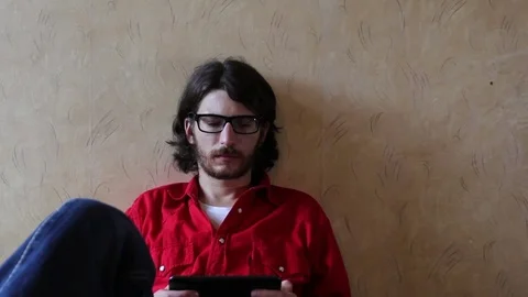 A young man with a gadget lying on sofa in his room 動画素材 82211112