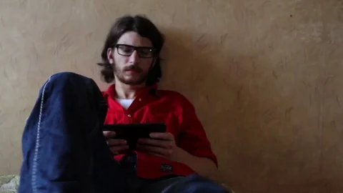 A young man with a gadget lying on sofa in his room 動画素材 82211123