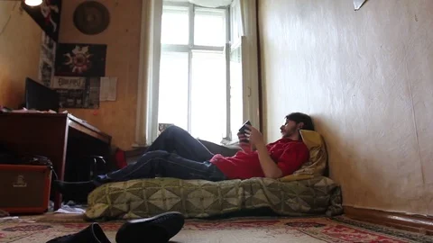 A young man with a gadget lying on sofa in his room (dolly shot) 動画素材 82211151