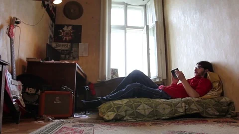 A young man with a gadget lying on sofa in his room (dolly shot) 動画素材 82211158