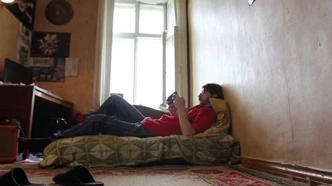 A young man with a gadget lying on sofa in his room (dolly shot) 動画素材 82211197