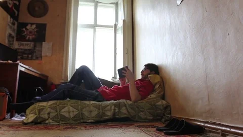 A young man with a gadget lying on sofa in his room (dolly shot) 動画素材 82211222