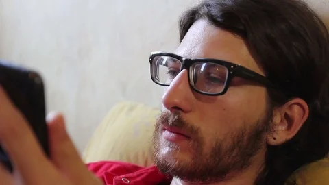 A young man with a gadget lying on sofa in his room 動画素材 82211288