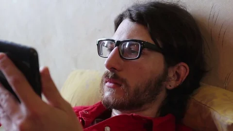 A young man with a gadget lying on sofa in his room Video stock 82211311