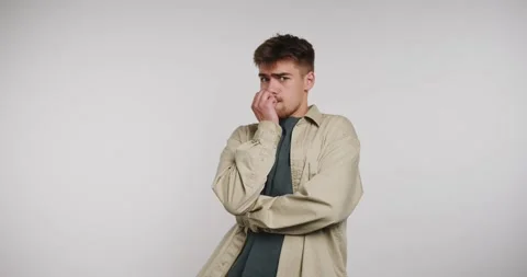 Young man gestures and thinks deeply while standing indoors in a simple set.. Vídeo Stock 326788351