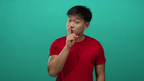 Young man gestures silence with finger on lips against isolated green backg.. Stock Footage 308585123
