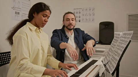 Young Man Gesturing and Explaining Rhythm to Teenager at Piano Stock Footage 339195810