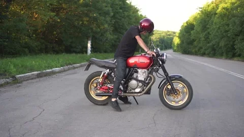 A young man gets on a cafe racer motorcycle and rides on the road Stock Footage 140044295