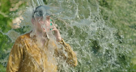 Young man getting doused with a bucket of water while on a phone call Stock Footage 279724115
