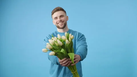 Young man gives bunch of white tulips on blue background Stock Footage 266459948