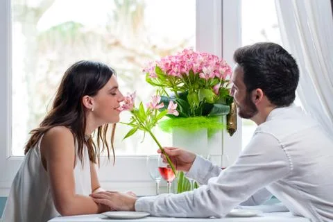 Young man giving flower to girlfriend in restaurant. Stock Photos