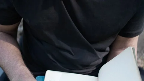 Young man glancing through a notebook seated in park, 스톡 동영상 287491785