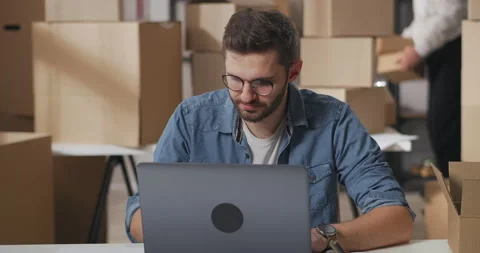 Young man with glasses and a beard takes the goods out of the box. Small Stock Footage 149471904