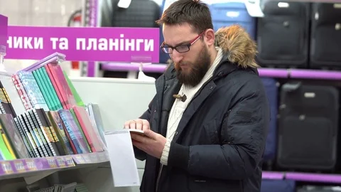A young man in glasses chooses notebook in the supermarket Stock Footage 71946616