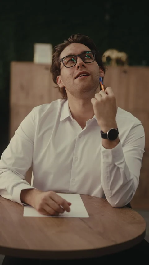 Young man with glasses has idea, thinking deeply, smiling and writing with pen Stock Footage 342935583