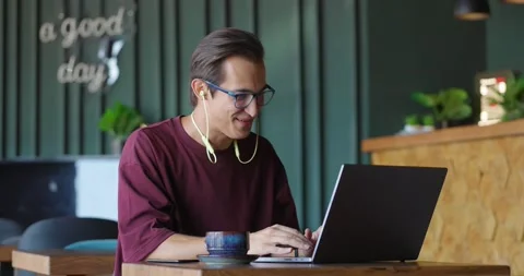 Young man in glasses having a video call on laptop while sitting at a cafe. Man 스톡 동영상 163900962