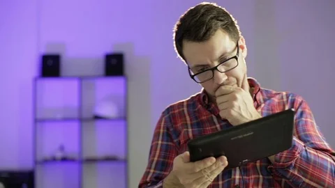 A young man in glasses holding a tablet in  hands and  looking for information o Stock Footage 70903844