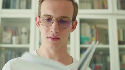 Young man with glasses reading a book in a library. Video stock 334848765
