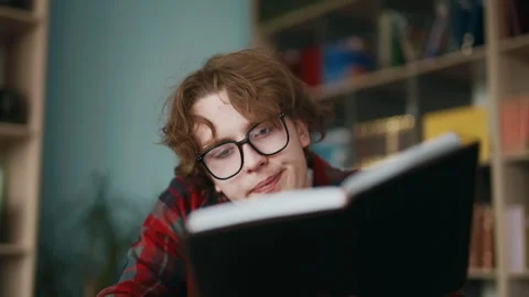 Young man with glasses reading a book in a library studying indoors Stock Footage 343555879
