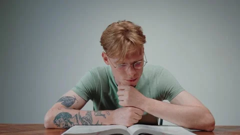 Young man in glasses reading a textbook and stressing, with his fist in his chin Vídeo Stock 164372302