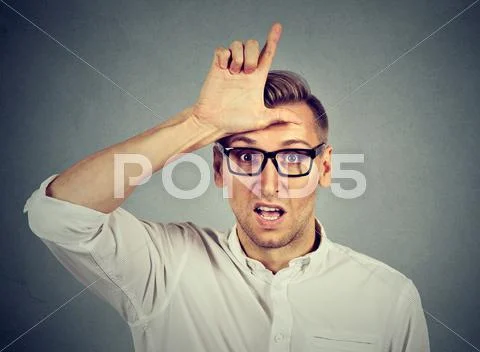 Young man in glasses showing loser sign on forehead Stock Photos