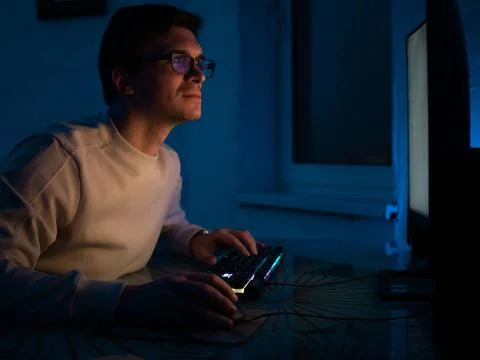 Young man with glasses sits at a computer and is engaged in programming, Foto stock