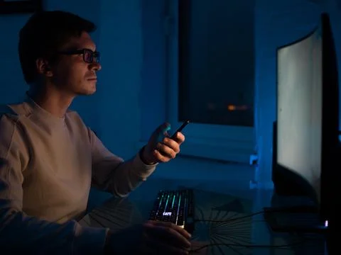 Young man with glasses is sitting at a computer and working on an online project Foto stock