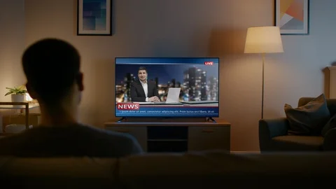 Young Man in Glasses is Sitting on a Sofa and Watching TV with Live News. Stock Footage 102492665