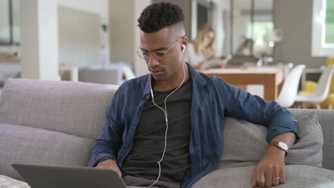Young man with glasses sitting in sofa at home and watching video with laptop Stock Footage 144606719