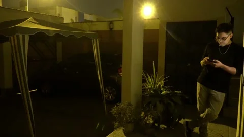 A young man with glasses standing leaning on the wall of the garage of his house Видео 160378968