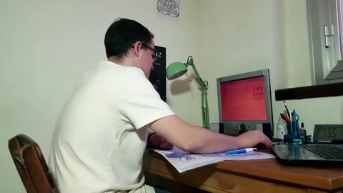 Young man with glasses studying concentrated at his desk with his computer Stock Footage 243126451