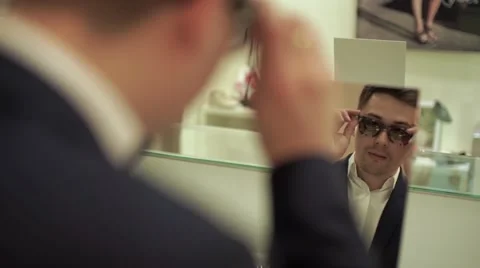 Young man with glasses try dark sun glasses in shopping mall Video stock 65540514