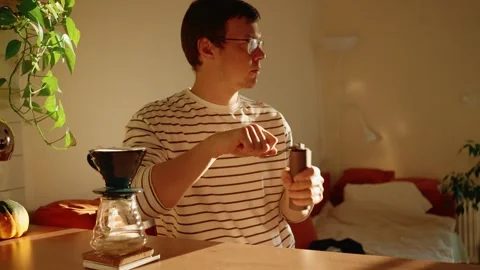 Young man with glasses using a manual coffee grinder for his morning routine in Stock Footage 347161038