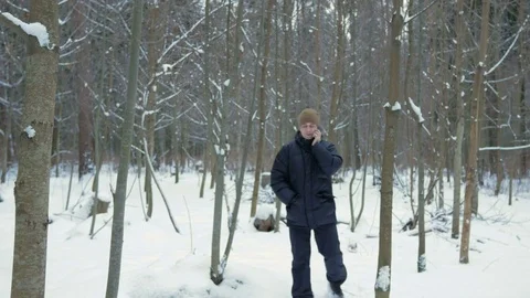 A young man goes on a winter forest and talking on the phone. He stops and ends Stock Footage 71206311