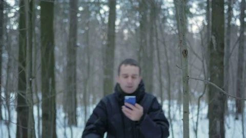 The young man goes in the winter forest and is oriented over the phone. He is Stock Footage 71213640