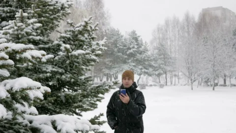 The young man goes in a winter forest in the snow and is oriented over the phone Stock Footage 71215264