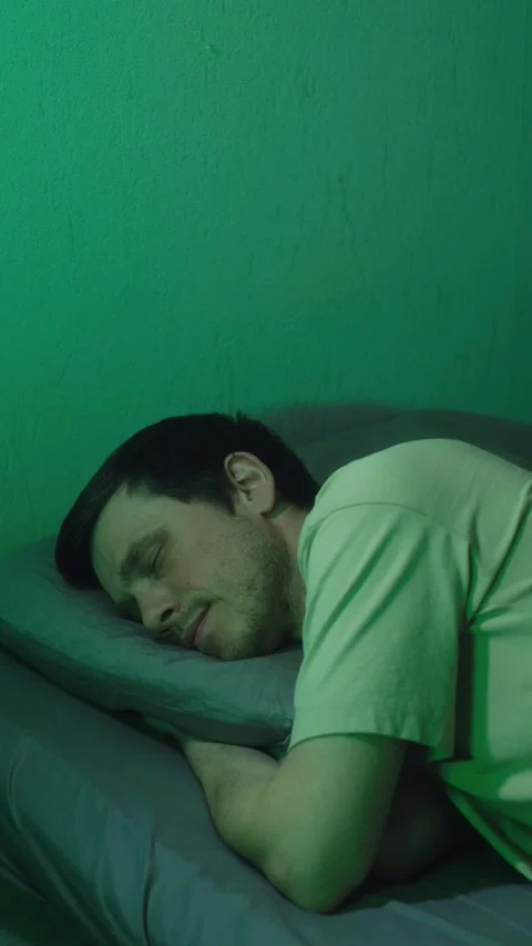 Young man going to sleep in a dark green room 스톡 동영상 337892922